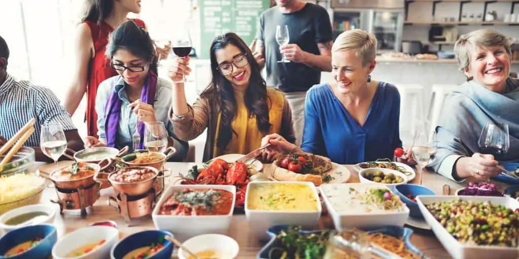 group of friends and family eating at table with main dish recipes for large groups