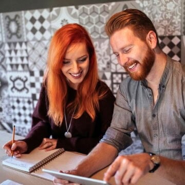 couple budgeting with an app on tablet and with paper, smiling