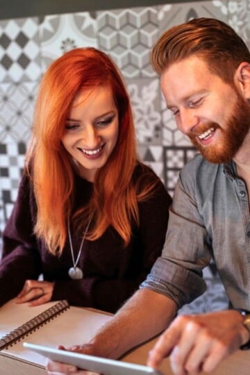 couple budgeting with an app on tablet and with paper, smiling