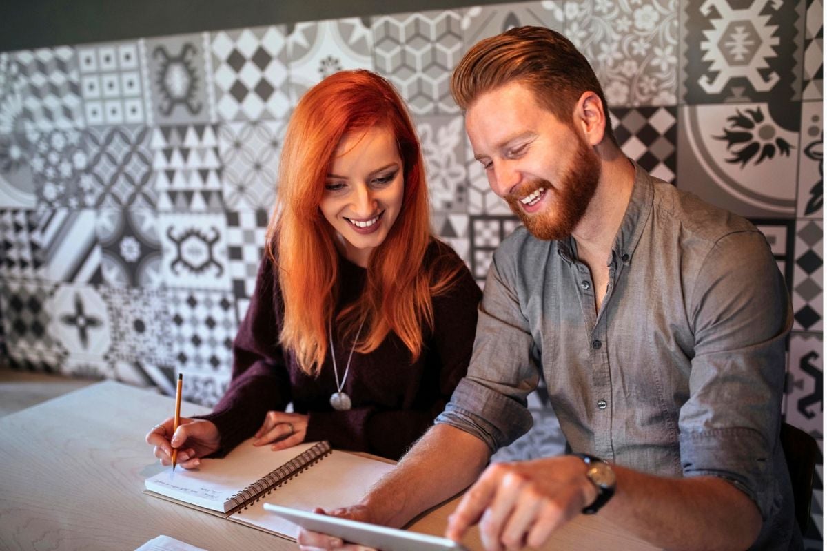 couple budgeting with an app on tablet and with paper, smiling