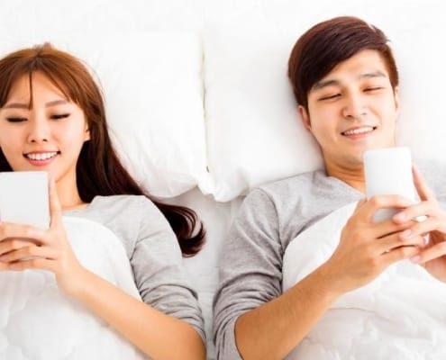 married couple in bed with smartphones, not talking, wondering how to emotionally connect with spouse