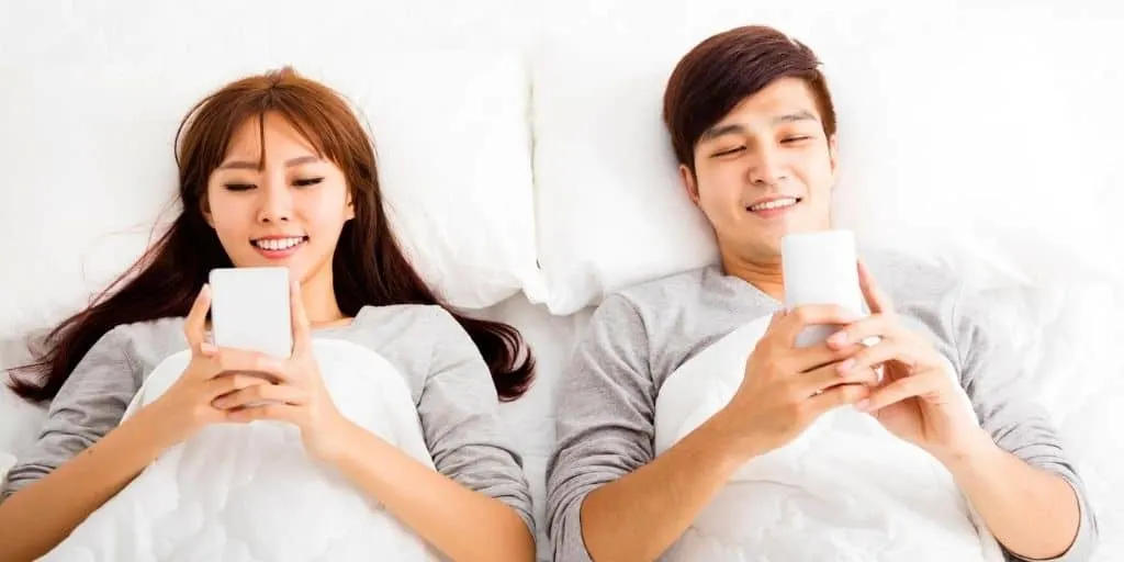 married couple in bed with smartphones, not talking, wondering how to emotionally connect with spouse