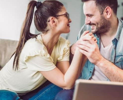 married couple on couch smiling at each other getting ready for weeknight date idea