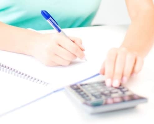 woman in blue shirt at desk, working on budgeting techniques and strategies with calculator