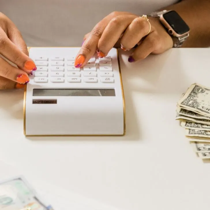 woman's hands using gold and white calculator with money on white table