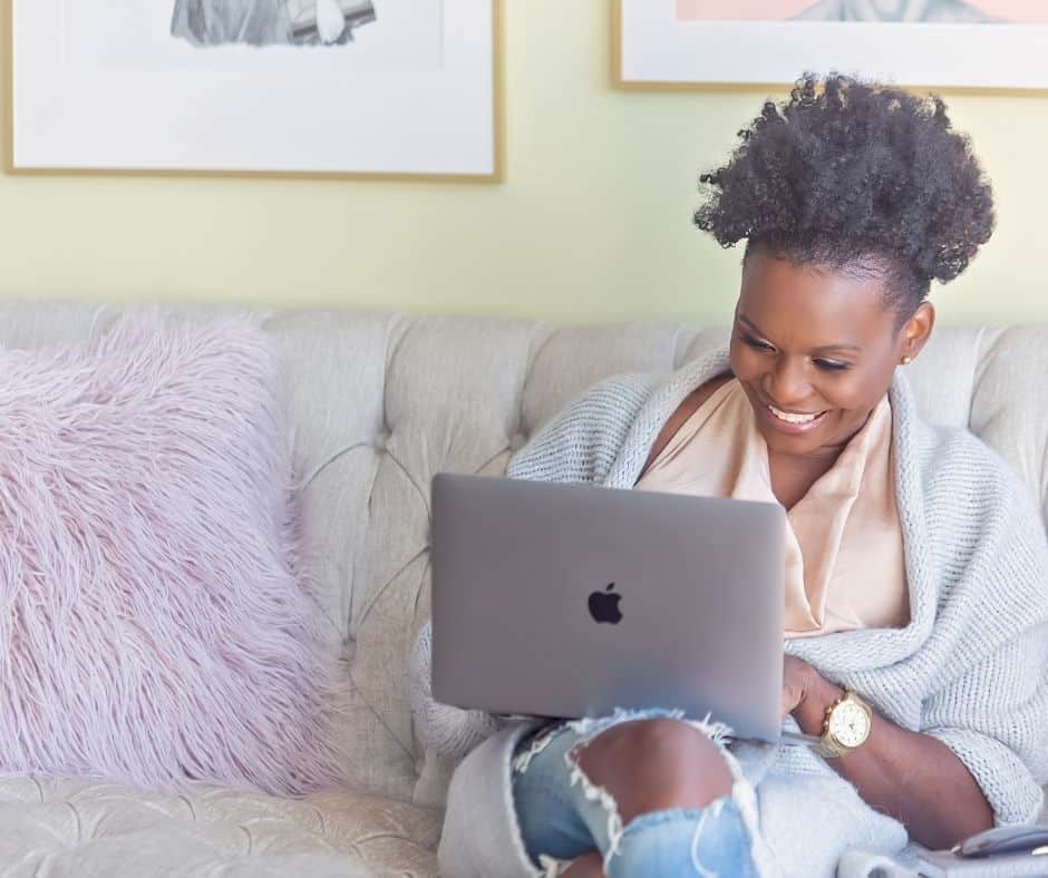 woman smiling on laptop on sofa with purple pillow, finding ways for how do you stop spending online