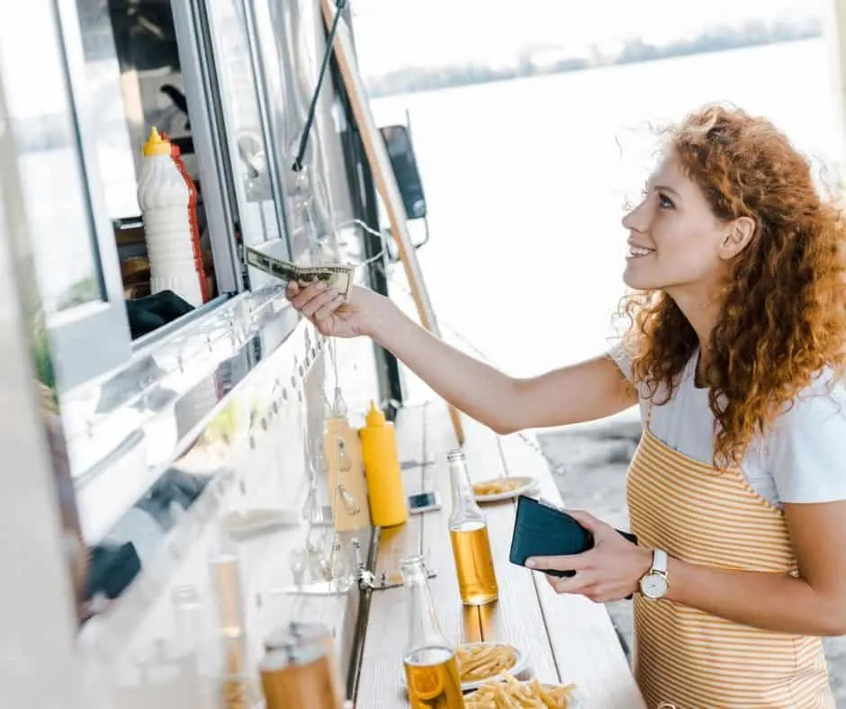 woman handing money to someone in a food truck, thinking about How to Spend Less Money on Food