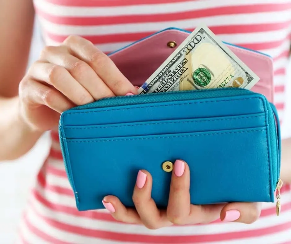 woman in striped shirt with wallet and money, checking in with her finances to help how to stop spending money you don't have