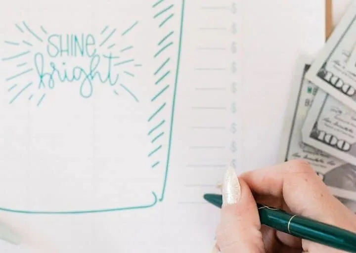 money on desk next to woman's hand writing on emergency fund tracker printable