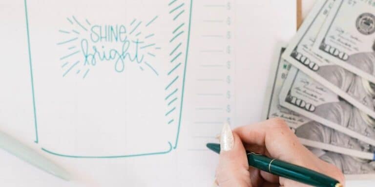 money on desk next to woman's hand writing on emergency fund tracker printable
