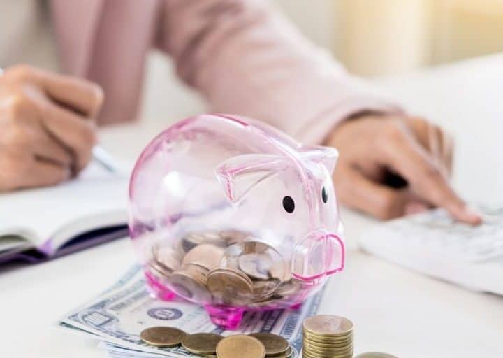 woman with pink piggy bank and calculator on desk, working on a no spend challenge rules list