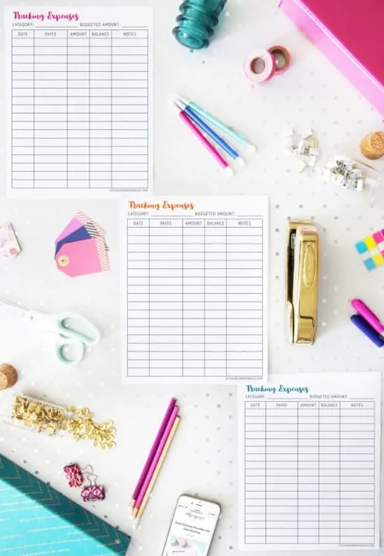 three monthly expenses trackers on white desk with lots of colorful elements like pens and staplers and stickers
