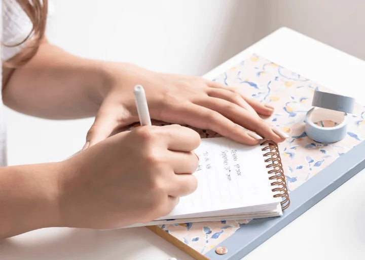 woman sitting at white desk filling in daily spending log printable