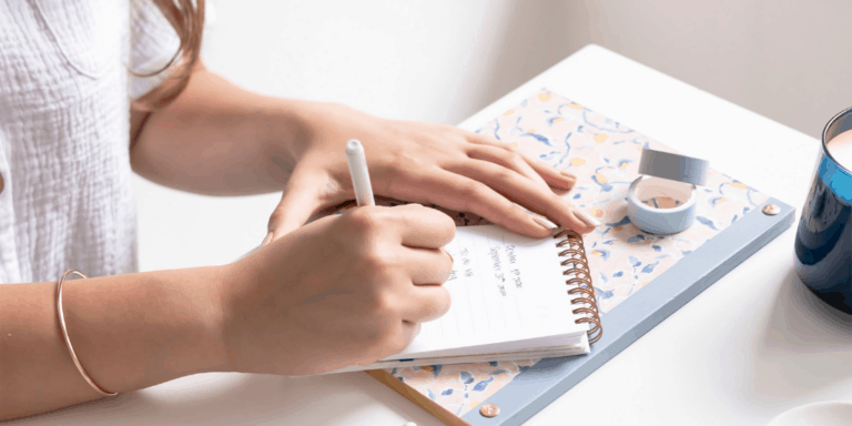 woman sitting at white desk filling in daily spending log printable