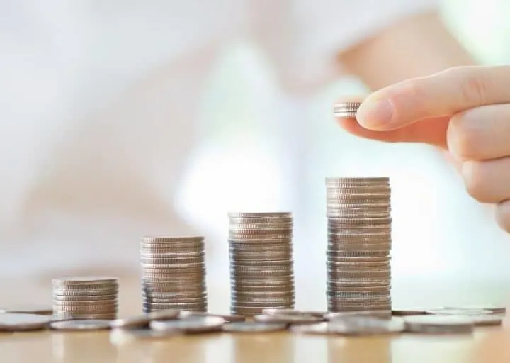 a hand counting a several towers of quarters on a wooden table, saving money on low paying job