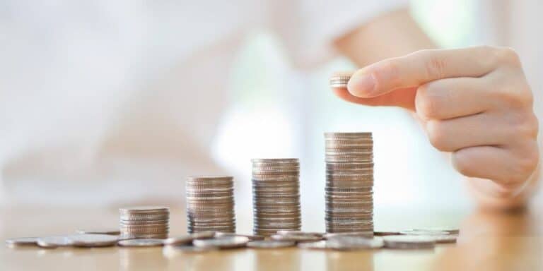 a hand counting a several towers of quarters on a wooden table, saving money on low paying job