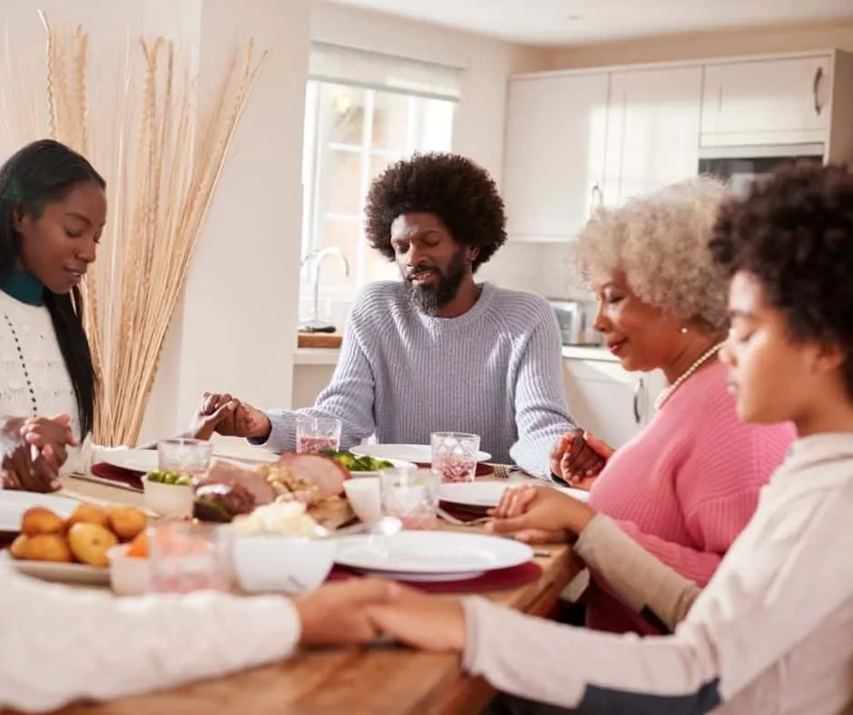 family sitting down to family Sunday dinner, holding hands while praying