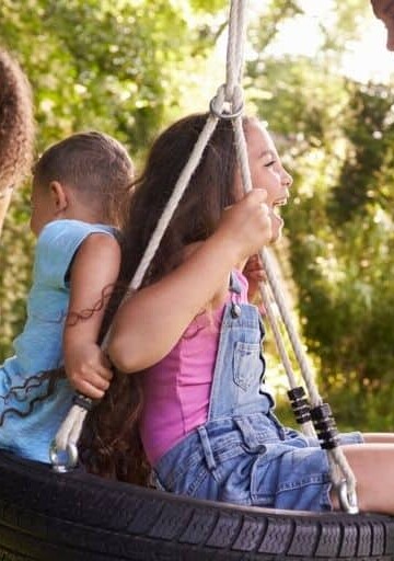 family of four laughing and playing on a tire swing out back as a way to cut family expenses