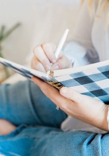 woman in jeans on bed writing her smart financial goals in journal