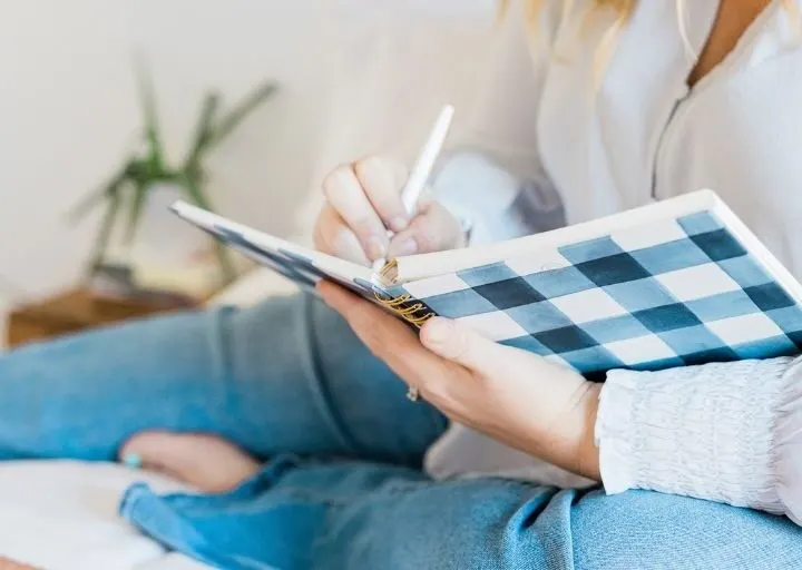 woman in jeans on bed writing her smart financial goals in journal