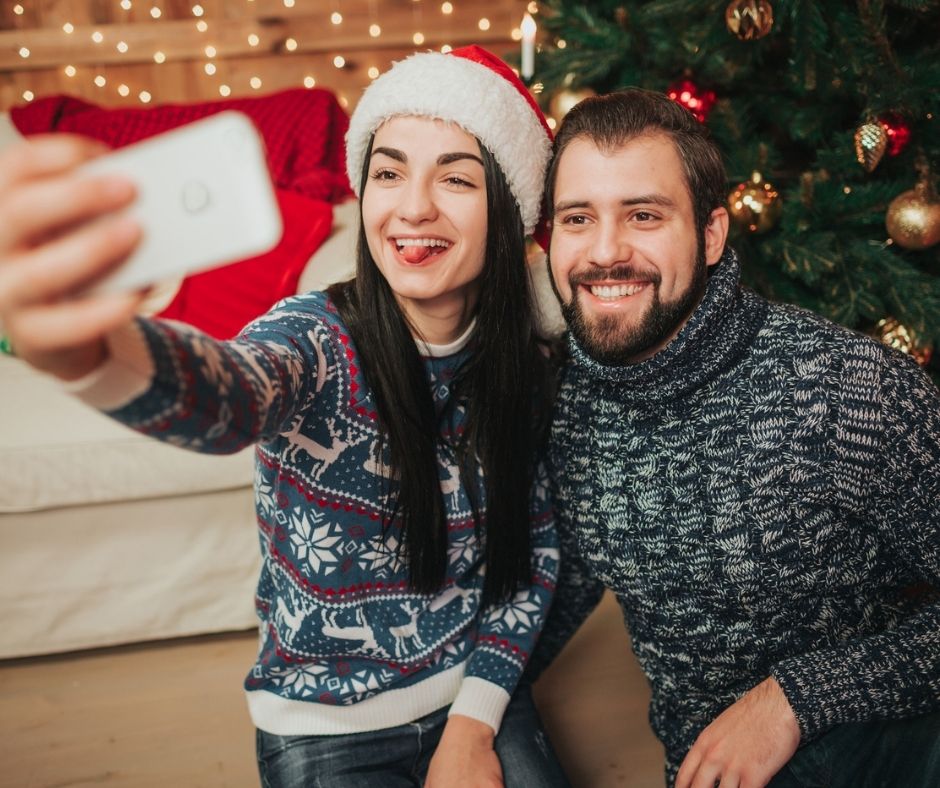 couple with Santa hat, taking selfie in front of tree after playing Santa claus