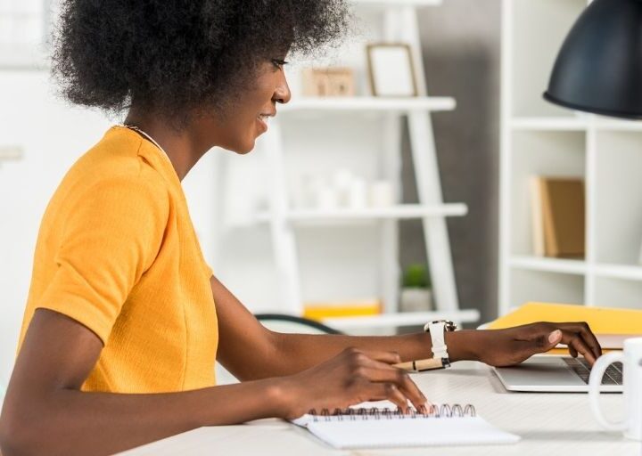 young woman in yellow shirt at desk, thinking about which financial goal category she wants to go after