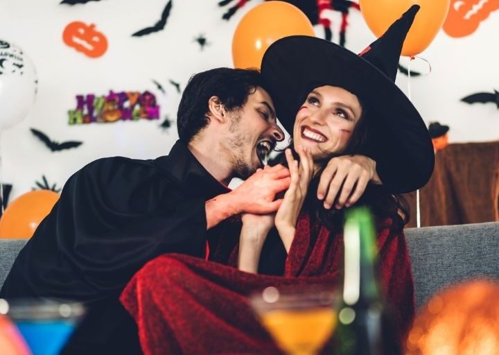 adult couple on couch dressed in Halloween costumes, giggling for things adults can do for halloween