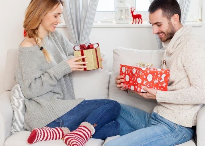 couple exchanging Christmas eve boxes for adults on white couch