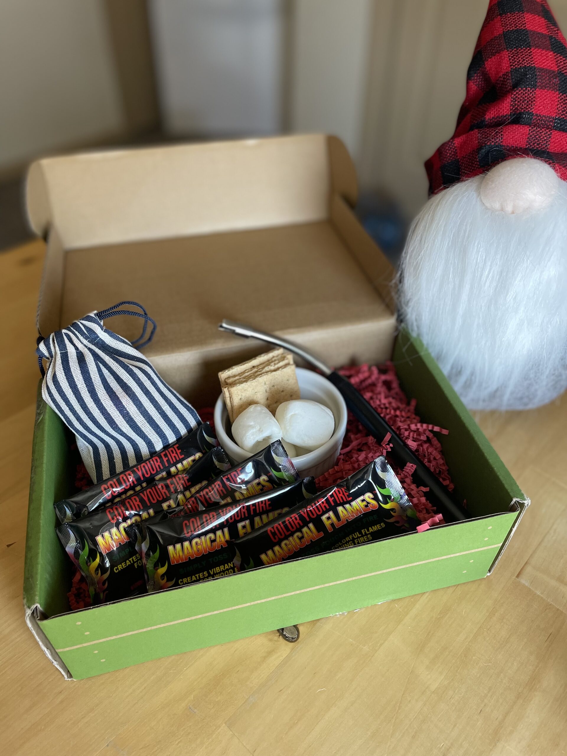 green box with red stuffing, arc fire lighter, treat sack, fire colorant packages, and marshmallows and graham crackers in a little ramekin