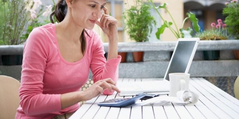 young woman in pink shirt at laptop with calculator, smiling about mini savings challenges