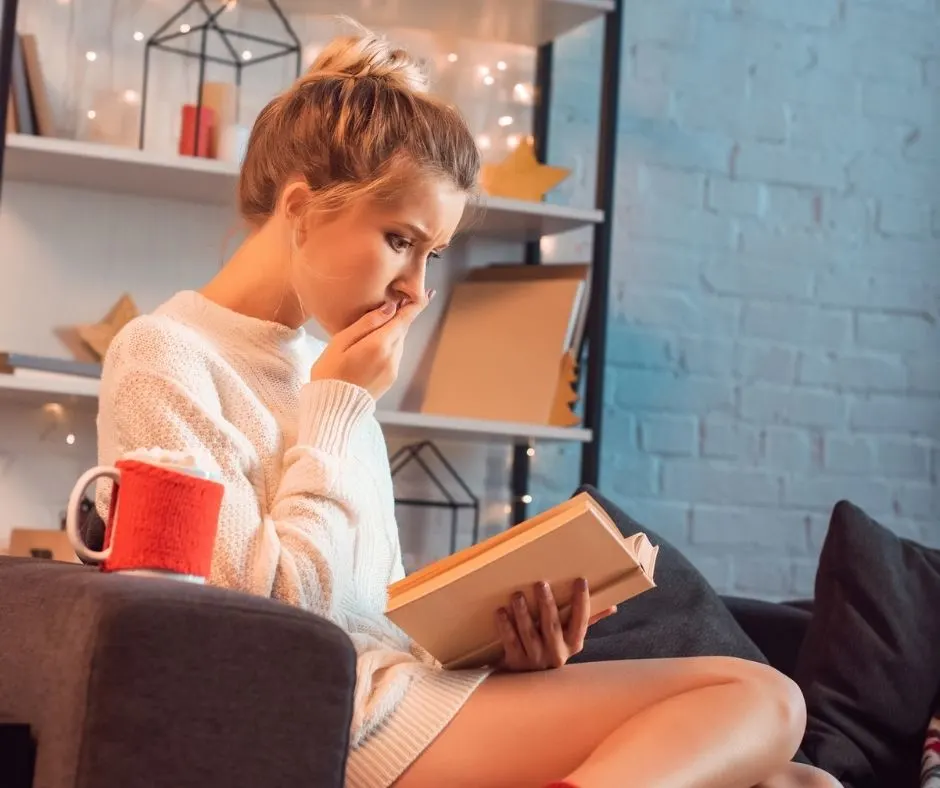 girl reading spooky book on couch, looking shocked