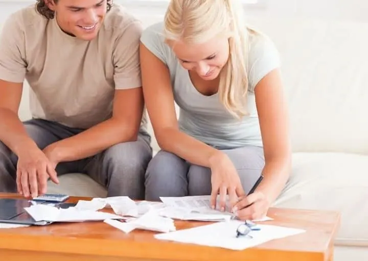 young couple working on printable for how to get one month ahead on bills, smiling