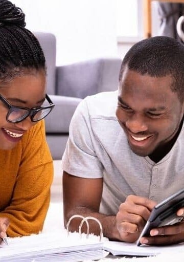 couple on floor working on budget to go from two incomes to one, smiling