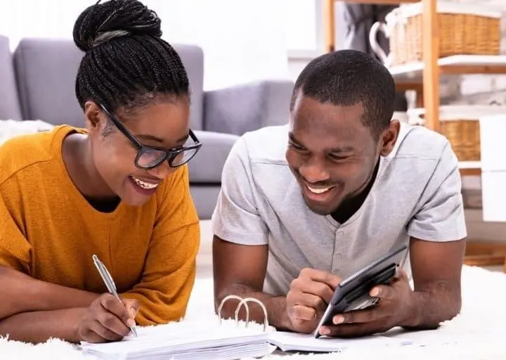 couple on floor working on budget to go from two incomes to one, smiling