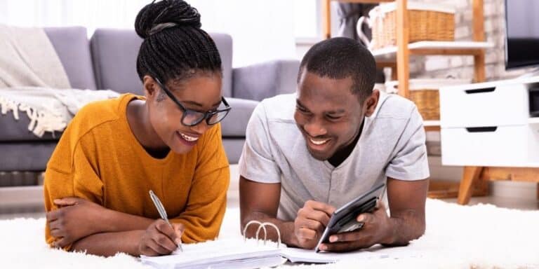 couple on floor working on budget to go from two incomes to one, smiling