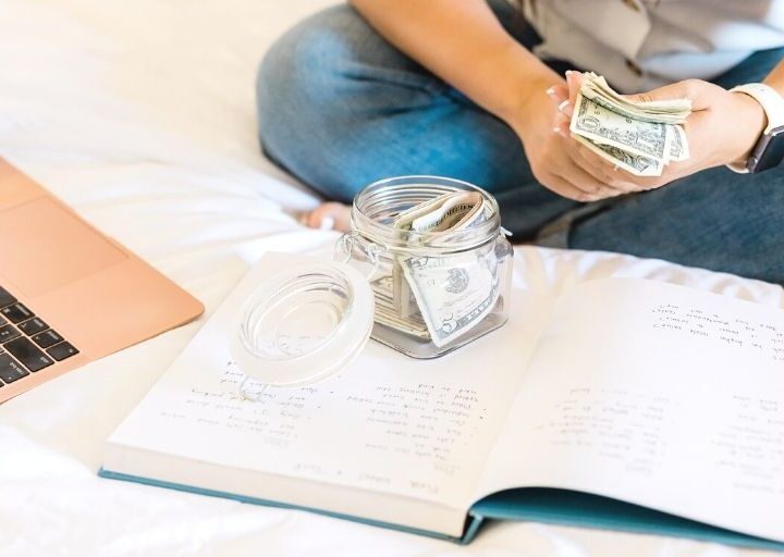woman in blue jeans on bed, counting money towards realistic savings goal