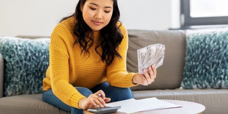 young woman in orange sweater with money calculating daily money saving challenge amount