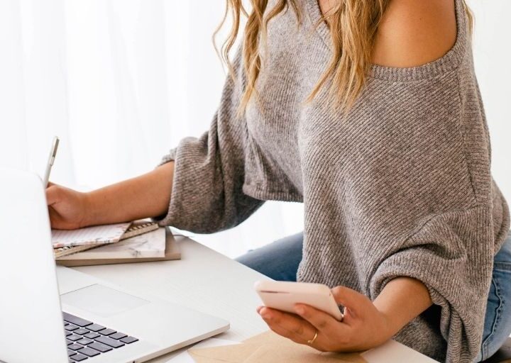 woman in sweater at desk with calculator on phone, working on sinking funds tracker pdf