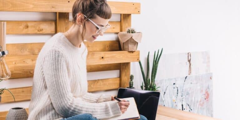 woman with glasses on bed, tracking her money on paper, and smiling
