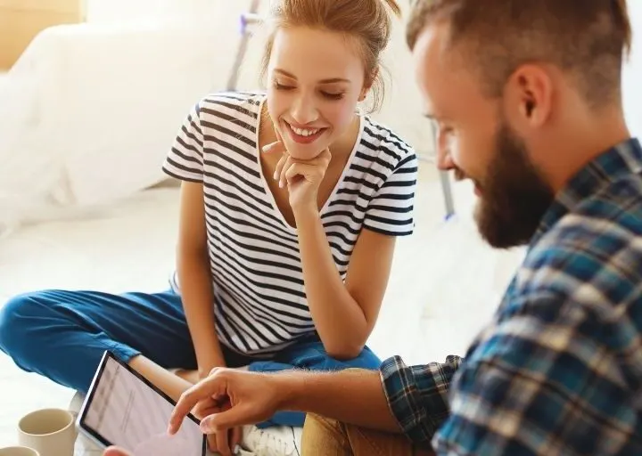 couple having fun looking at tablet that has money saving challenges for couples on it