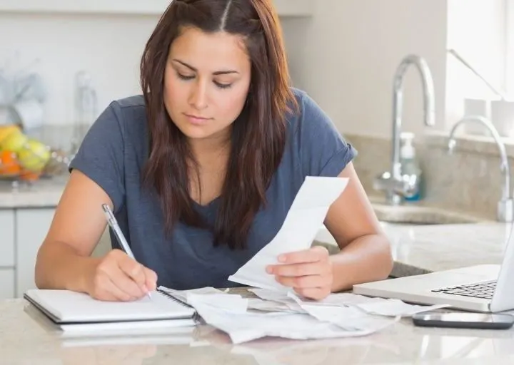 woman sitting at kitchen bar, checking off bills she's paid on printable bill pay checklist pdf