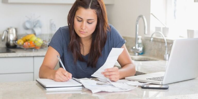 woman sitting at kitchen bar, checking off bills she's paid on printable bill pay checklist pdf