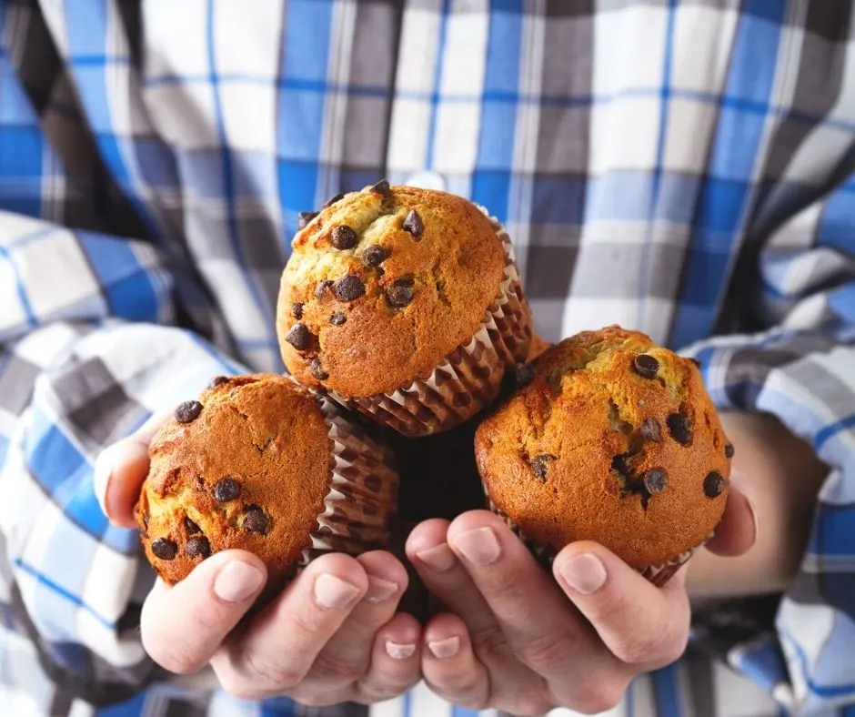 man in flannel shirt holding three banana protein chocolate chip muffins