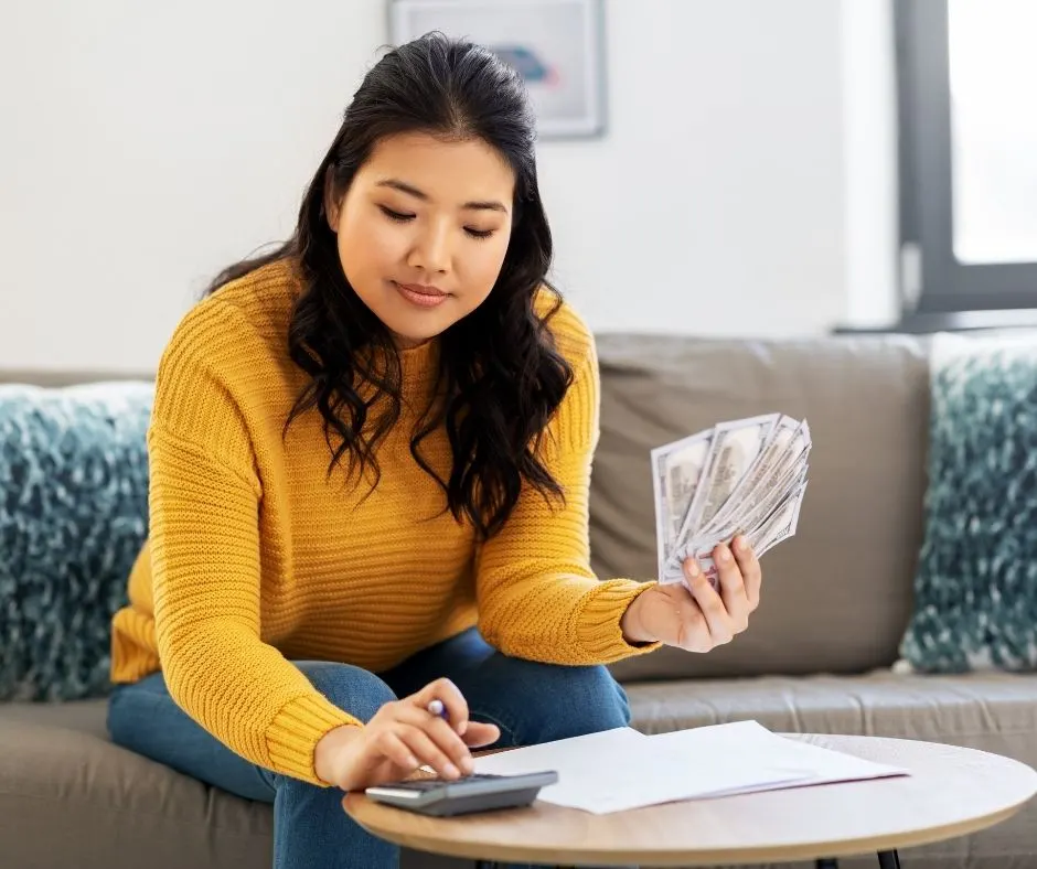 woman in orange sweater with cash in hand, working on a cash budget