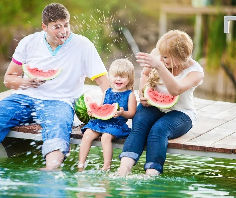 family of three eating watermelon and splashing each other off a dock