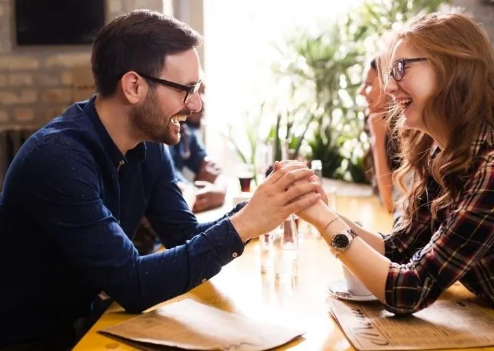 couple with glasses, on a coffee shop date, smiling at each other