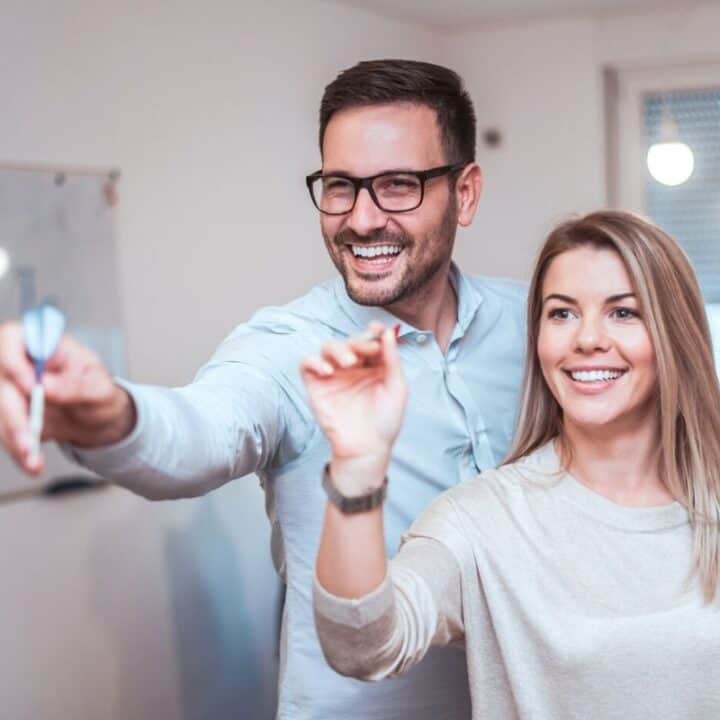 couple playing darts, thinking about meeting savings goals