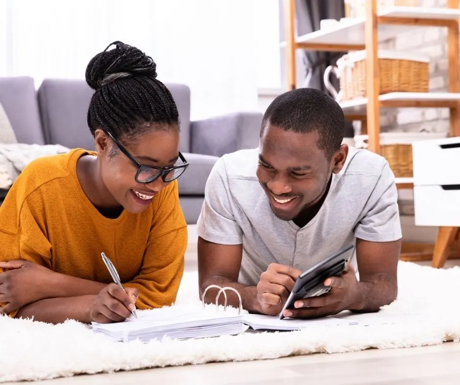 young couple with calculator and notepad on floor, having fun figuring out frugal strategy and finances