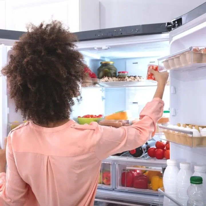 woman in peach-colored shirt reaching into fridge to figure out how to reuse leftovers