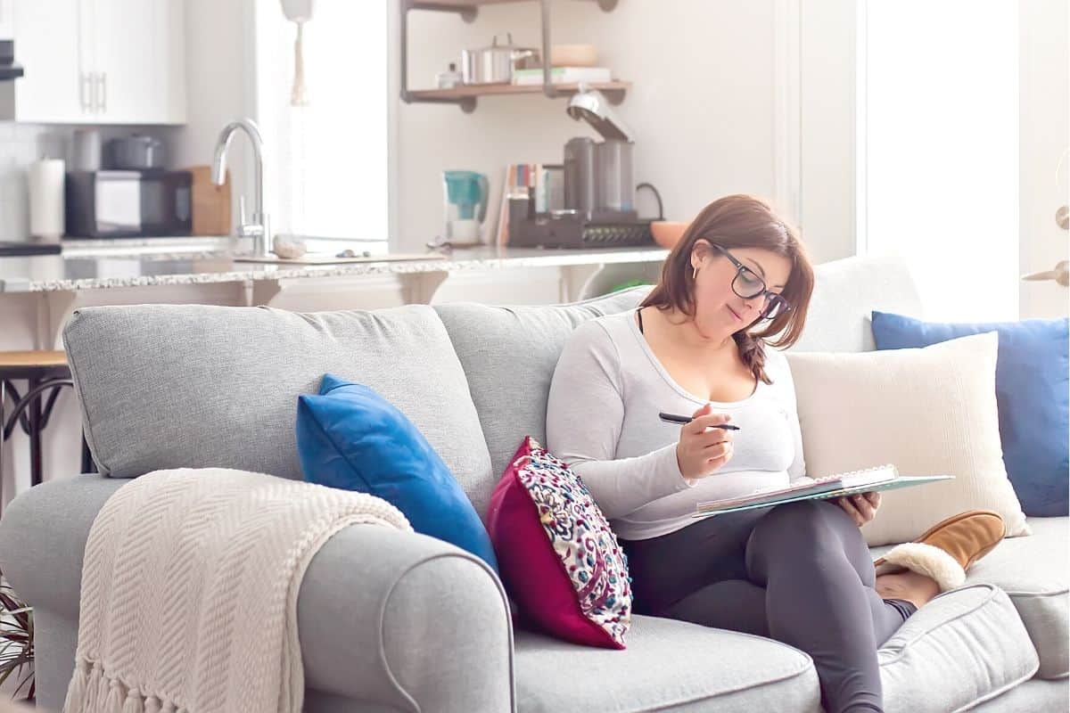 woman in glasses on couch, working on writing out her savings challenge